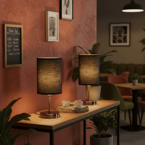 Two antique brass table lamps with black shades on a wooden console table, surrounded by plants and decor.