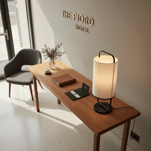 Watson Black & White Cylinder Table Lamp on a wooden table in a hotel lobby setting.