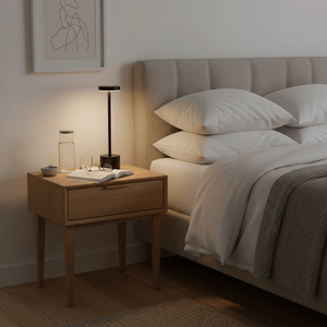 Modern black rechargeable table lamp on a bedside table with a book, glasses, and a water bottle.