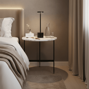 Modern black rechargeable table lamp on a marble side table beside a bed, with decorative items and soft lighting.