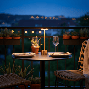 Rechargeable gold table lamp on a balcony table set for dinner, surrounded by potted plants.
