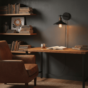 A retro-industrial wall reading light mounted above a wooden desk with books and a coffee mug.