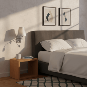 Polished chrome wall light with silver thread shade mounted beside a bed, casting soft light.