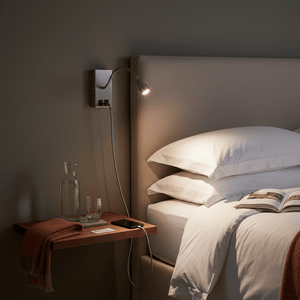 Satin chrome wall‑mounted reading light with flexible gooseneck, base with outlets and USB, illuminated beside bed headboard