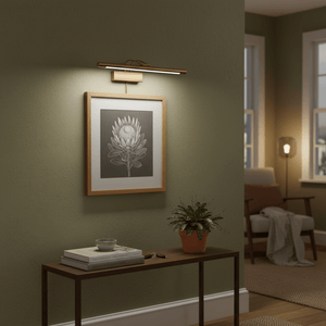 Antique bronze picture light illuminating a framed artwork above a console table in a cozy indoor setting.