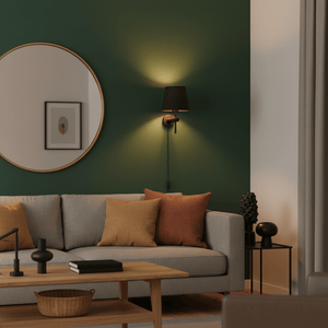 Dahlia Wall Light in antique brass mounted beside a round mirror on a green wall, illuminating a cozy living room.