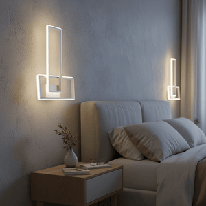 White rectangular LED wall sconce on textured wall, glowing warm light, beside a bed and nightstand with vase and books.