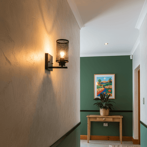 Up-facing wall light with metal mesh shade illuminating a hallway, featuring green walls and a decorative table.