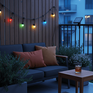 Colorful solar string lights illuminate a cozy patio setting with cushions and a drink.