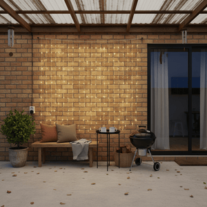 Warm white LED curtain lights hang across a brick patio wall beside a bench, table, grill and glass door.