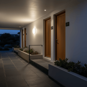 Nighttime exterior hallway with wooden doors 07 and 25, illuminated by a round white wall light, tiled floor, and planters