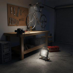 A portable worklight illuminating a garage workspace with tools and a bicycle in the background.