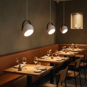 Three white leather strap pendant lights illuminating a cozy restaurant dining area with wooden tables and brown seating.