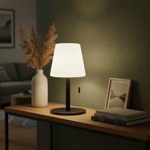 A modern rechargeable table lamp with a soft white shade on a wooden table, surrounded by decor items.