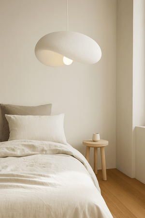 Ivory Drift 700 Pendant Light hanging above a bed with neutral bedding and a wooden side table.