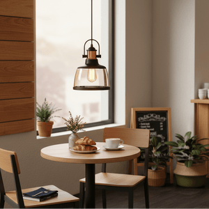 Metal pendant light with cognac glass hanging above a wooden dining table with croissants and coffee.