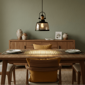 Metal pendant light with cognac glass hanging above a wooden dining table set with plates and a yellow cushion.