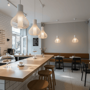 Scandi white pendant lights hanging in a modern café setting, illuminating a wooden counter and seating area.