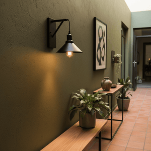 Caledon Black Indoor Wall Light mounted on a textured green wall, illuminating a hallway with plants and decor.