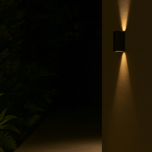 Wall-mounted outdoor light fixture casting a warm glow on a dark wall with plants in the background.