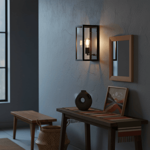 Metal indoor wall light with clear glass mounted beside a wooden table and mirror, illuminating the space.