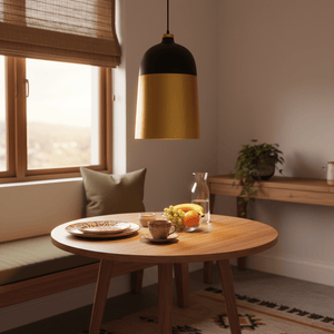 Two-tone black and gold pendant light hanging over a wooden dining table set with plates and fruits.
