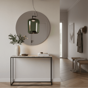 Green glass pendant light hanging above a console table with a vase and books, reflecting in a round mirror.