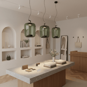 Three green glass pendant lights hang over a stylish display table in a modern retail space.