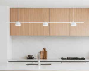 Modern kitchen with wooden cabinets, white countertops, and pendant lights.