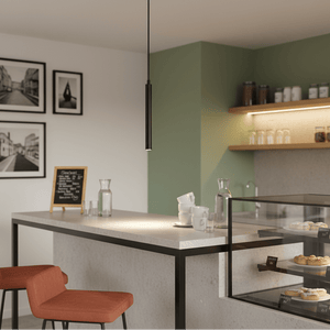 Slim LED pendant light hanging above a modern kitchen island with orange chairs and a display case.