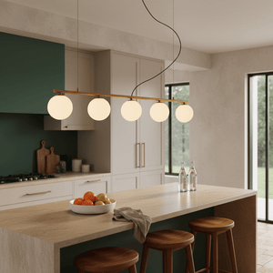 Linear pendant light with five glass shades hanging above a kitchen island, illuminating a bowl of fruit.