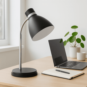 Gooseneck black metal desk lamp positioned on a wooden desk beside a laptop and notebook.