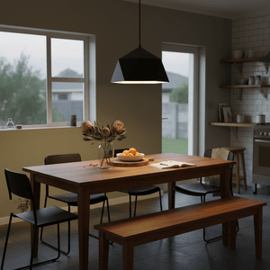 Black metal pendant light hanging over a wooden dining table with fruit and flowers, in a modern kitchen setting.