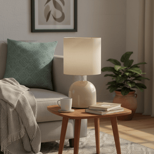 Beige metal table lamp with fabric shade on a wooden side table, beside a cozy sofa with a green cushion.