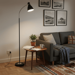 Black metal flexi head floor lamp beside a cozy couch, illuminating a reading area with a plant and coffee.