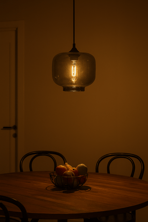Dining area with a round table, chairs, and a bowl of fruit under a hanging light fixture.