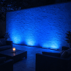 Outdoor setting with a textured wall illuminated by blue wall washer lights, featuring modern furniture.