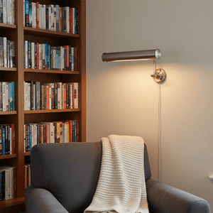 Antique silver wall lamp illuminating a cozy reading nook with a bookshelf and a grey couch.