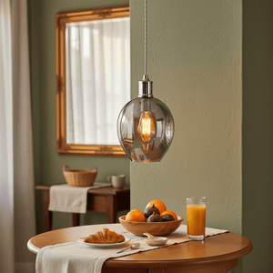 Polished chrome pendant light with glass shade hanging above a wooden table set with breakfast items.