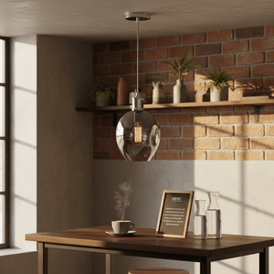Polished chrome pendant light with glass shade hanging above a wooden table with a coffee cup and decor.