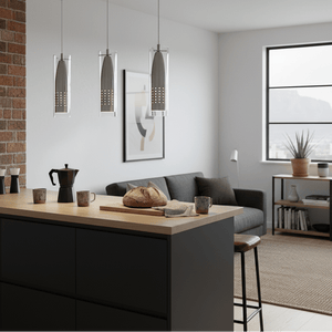 Three satin clear glass pendant lights hang over a kitchen island with bread and mugs.