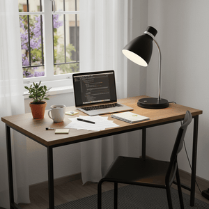 A black metal gooseneck desk lamp illuminating a workspace with a laptop, coffee cup, and stationery.