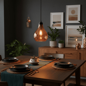 Rose copper glass pendant light hanging above a dining table set with black plates and a plant centerpiece.