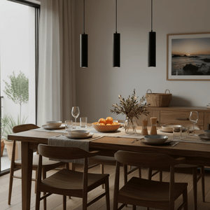 Three black cylindrical pendant lights over a dining table set with dishes and a fruit bowl.