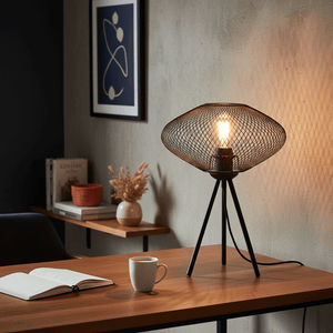 Stylish black mesh table lamp on a wooden desk with a coffee cup and an open book.