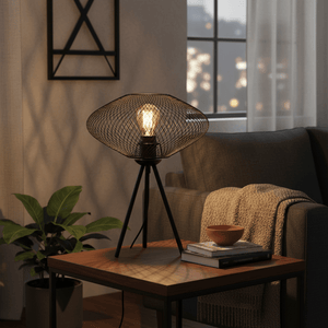 Black mesh table lamp on a wooden side table, casting warm light in a cozy lounge setting.