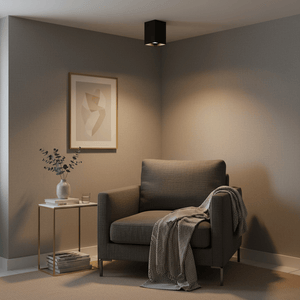 Modern black surface mount downlight illuminating a cozy living room corner with a chair and side table.