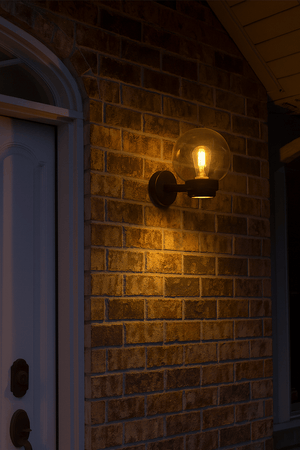 Black outdoor wall light mounted on a brick wall, illuminating the entrance with warm light.