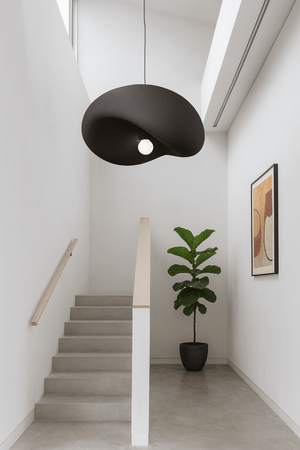 Obsidian Drift 700 Pendant Light hanging above a staircase, complemented by a potted plant and wall art.