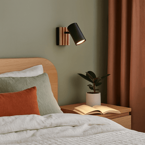 Bedroom with wooden headboard, pillows, and a nightstand with an open book and plant.
